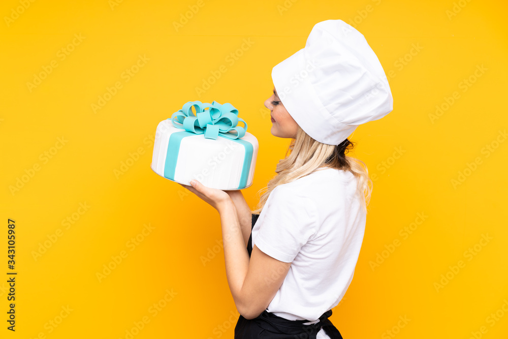 Teenager girl pastry holding a big cake isolated on yellow background Teenager girl pastry holding a big cake isolated on yellow background