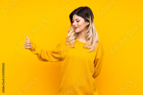 Teenager girl isolated on yellow background giving a thumbs up gesture