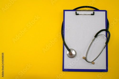 Stethoscope and purple folder-tablet on yellow background