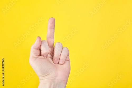 A female adult hand show middle finger on yellow background.