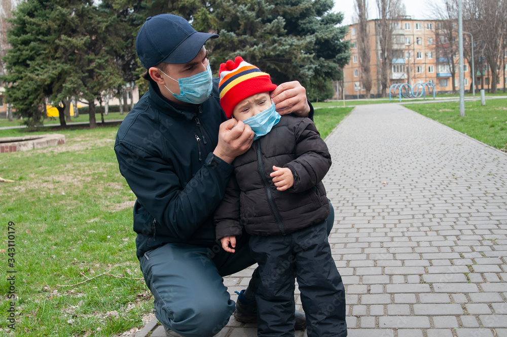 a man puts a medical mask on the child, as there are quarantines on the street and restrictions apply. The child breaks out and cries, does not want to wear