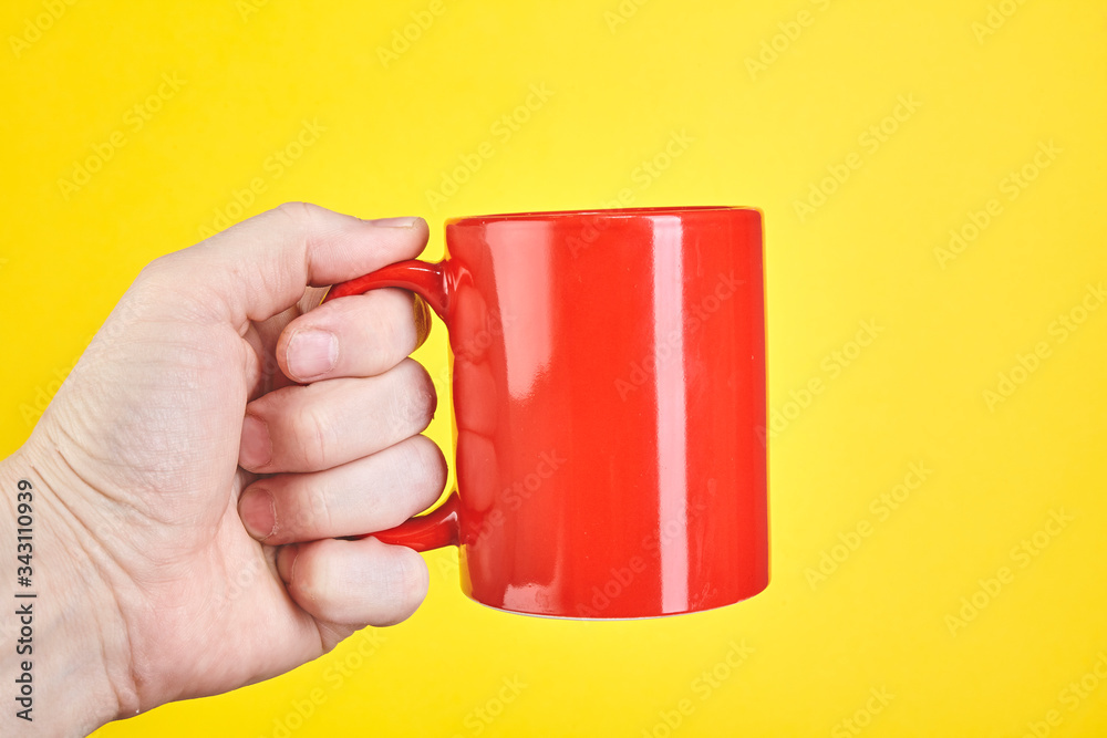 Obraz premium Male hand is holding a red cup isolated on a yellow background