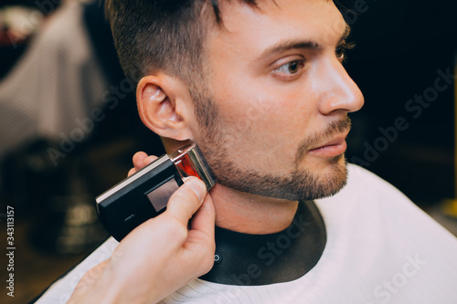 Portrait man being trimmed with professional electric clipper machine in barbershop.Male beauty treatment concept. guy getting new haircut in barber salon