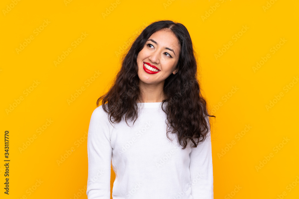 Mixed race woman over isolated yellow background laughing and looking up Mixed race woman over isolated yellow background laughing and looking up