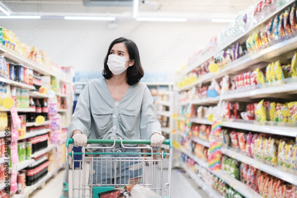 Asian woman wearing face mask and rubber glove push shopping cart in suppermarket departmentstore. Girl choosing, looking grocery things to buy at shelf during coronavirus crisis or covid19 outbreak. Asian woman wearing face mask and rubber glove push shopping cart in suppermarket departmentstore. Girl choosing, looking grocery things to buy at shelf during coronavirus crisis or covid19 outbreak.