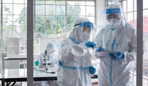 Scientists and microbiologists with PPE suit and face mask in lab calculate chemical formula to create vaccine or medicine for coronavirus infection. Covid-19, laboratory, and vaccine concept.