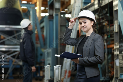 Portrait of a female factory manager in a white hard hat and business suit. Controlling the work process at the airplane manufacturer. 