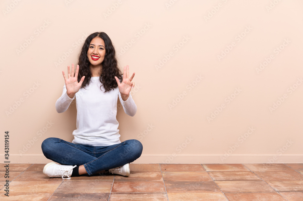 Young woman sitting on the floor counting nine with fingers Young woman sitting on the floor counting nine with fingers