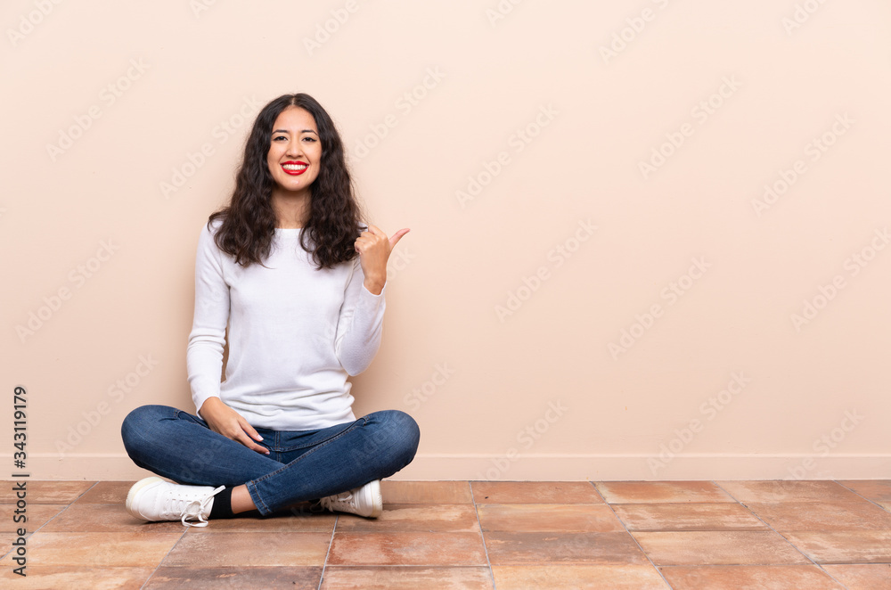 Young woman sitting on the floor pointing to the side to present a product Young woman sitting on the floor pointing to the side to present a product