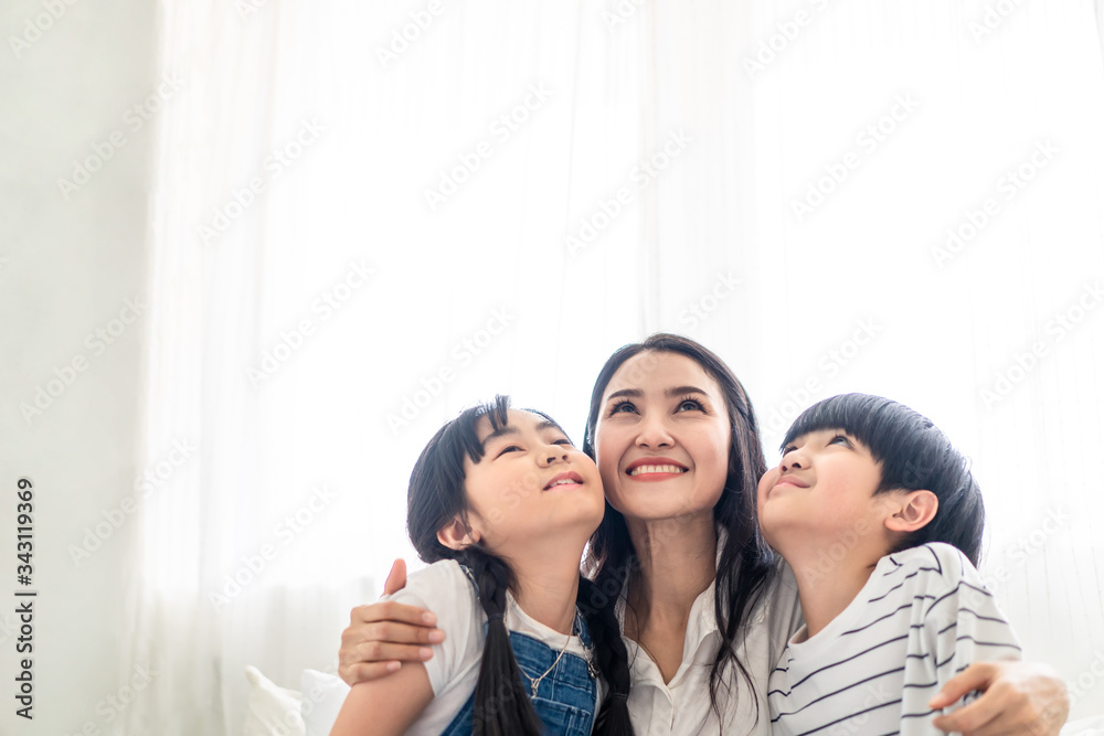 Asian family mother, son and daughter sit on white bed with happiness and smile in bedroom. Mom hug boy and girl playing together feeling fun. People look above. House property mortgage advertisement. Asian family mother, son and daughter sit on white bed with happiness and smile in bedroom. Mom hug boy and girl playing together feeling fun. People look above. House property mortgage advertisement.