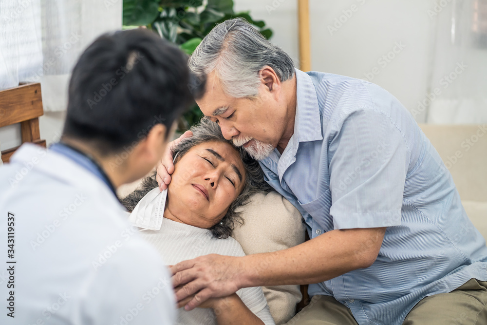 Asian senior old woman with bad condition feeling sick lying on sofa having medical check up by doctor visiting at home. Elder man husband taking care of wife closely and worry about unwell illness. Asian senior old woman with bad condition feeling sick lying on sofa having medical check up by doctor visiting at home. Elder man husband taking care of wife closely and worry about unwell illness.