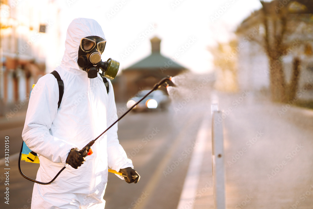 A man wearing special protective disinfection suit sprays sterilizer  in the empty public place at dawn in the city of quarantine. Covid -19. Cleaning concept.