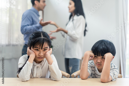 Two young children feeling sad and boring due to parents fighting at home. Older sister feels disappointed and sibling brother crying on father and mother aggressive trouble. Unhappy problem in family