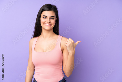 Young woman over isolated purple background pointing to the side to present a product © luismolinero