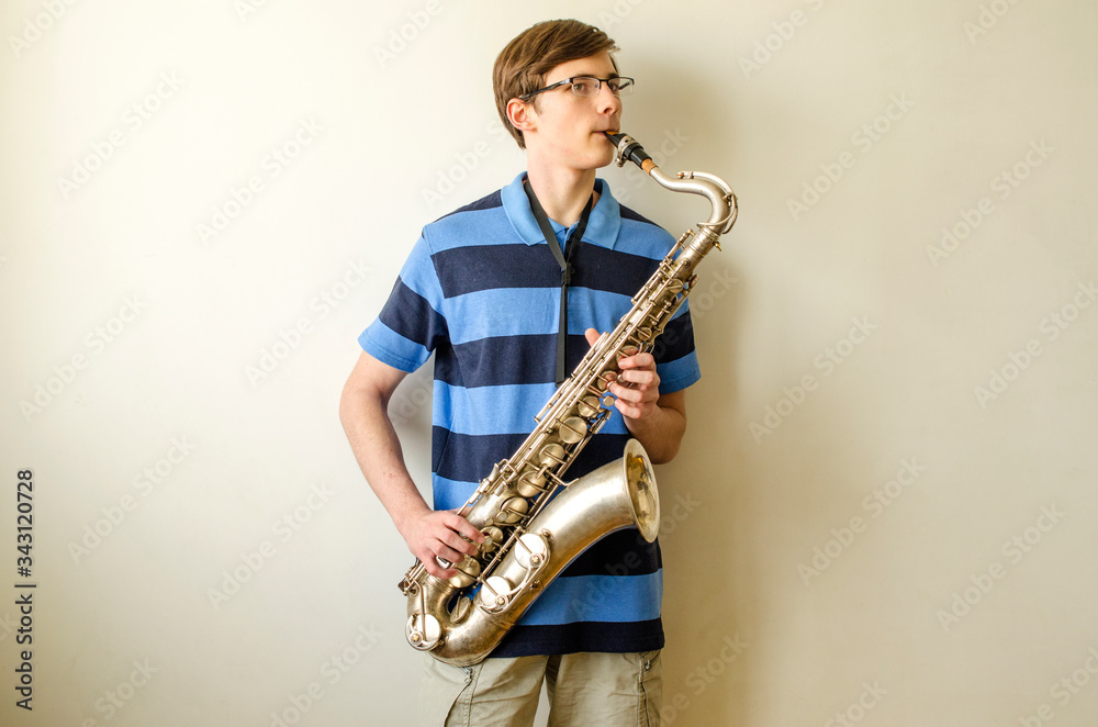 Naklejka premium Young saxophonist plays tenor saxophone in a striped blue shirt on a white background 