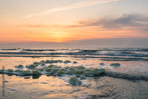 Sunset over the North Sea  seen from the dutch coast. Sea foam is washed ashore.