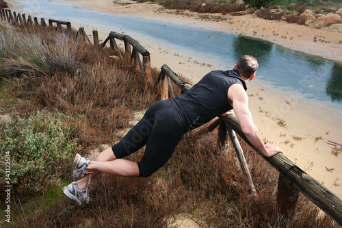 Uomo di mezza età sportivo fa stretching lungo il corso di un fiume su una ringhiera di legno photo