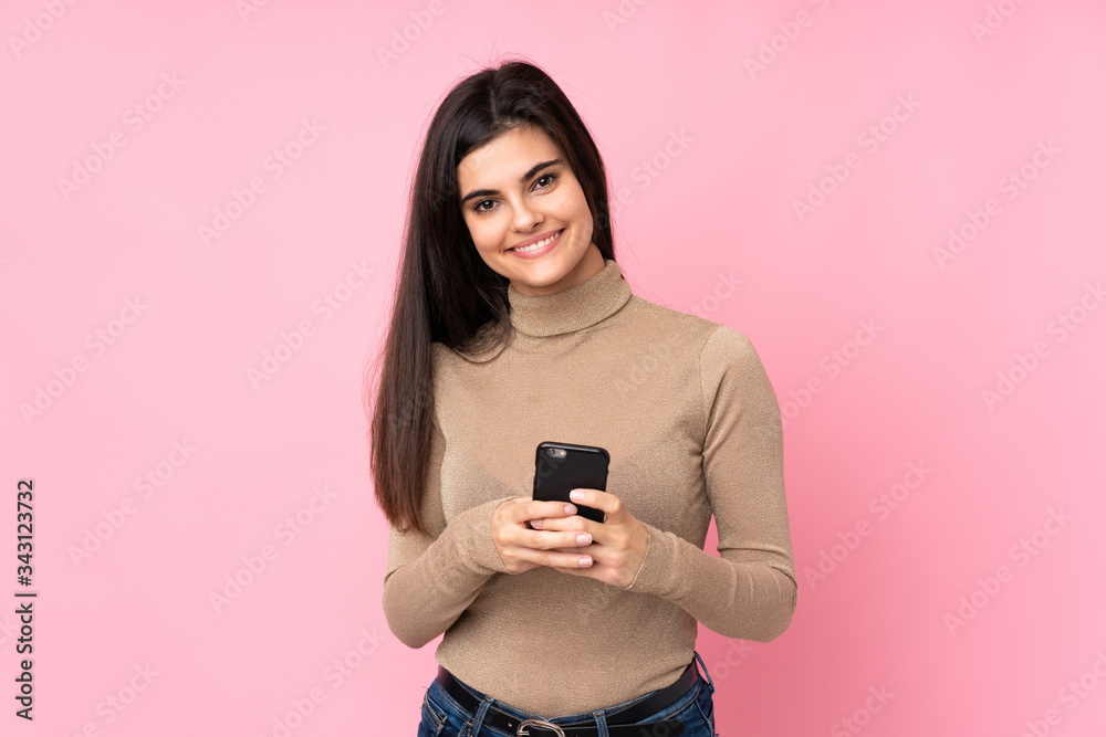 Young woman over isolated pink background sending a message with the mobile Young woman over isolated pink background sending a message with the mobile