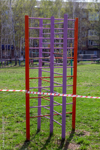 A white and red ribbon prohibits entry to the Playground. Playground swing in the open air prohibiting red tape  infection prevention