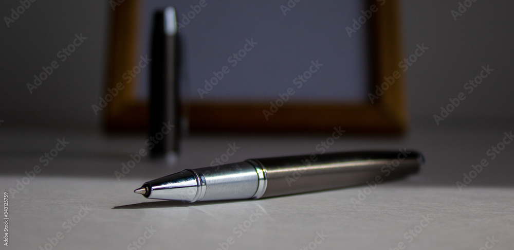 Pen on beautiful white fon on warm light. Wooden picture frame and cap in the background. Pen on beautiful white fon on warm light. Wooden picture frame and cap in the background.