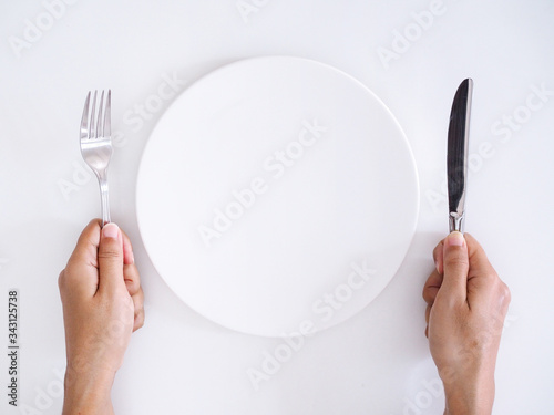 Top view of empty white ceramic plate with hand with knife and fork