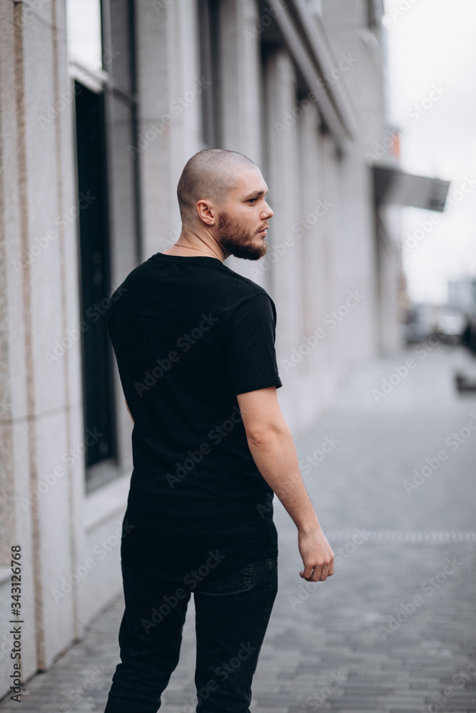Fototapeta premium portrait of a bald handsome bearded man in a black t-shirt on the street, who looks away