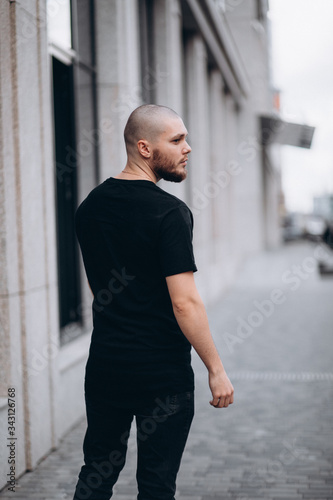 portrait of a bald handsome bearded man in a black t-shirt on the street, who looks away