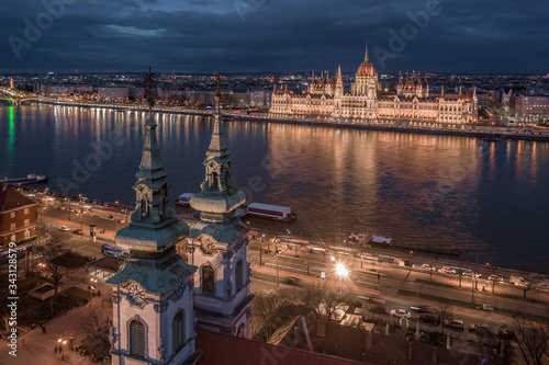 Budapest, Hungary - Aerial view of the Saint Anne Parish Church at Batthyany Square at dusk with illuminated Hungarian Parliament building and cloudy dark blue sky at background