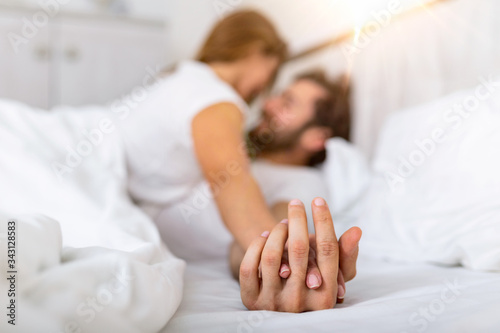 Romantic couple in bed enjoying sensual foreplay. Focus on hands man and woman. Happy sensual young couple lying in bed together. Beautiful loving couple kissing in bed.