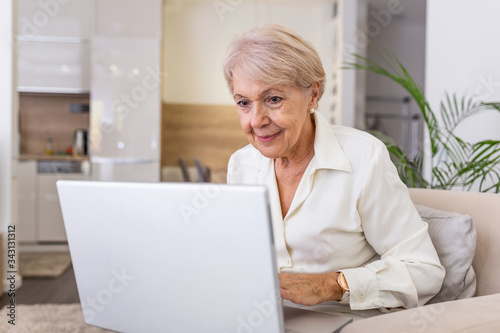 Elderly lady working with laptop. Portrait of beautiful older woman working laptop computer indoors. Senior woman using laptop at home  laughing