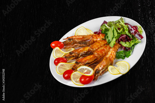 Shrimps, tomatoes and lemon are beautifully laid out on a dish on a black background.