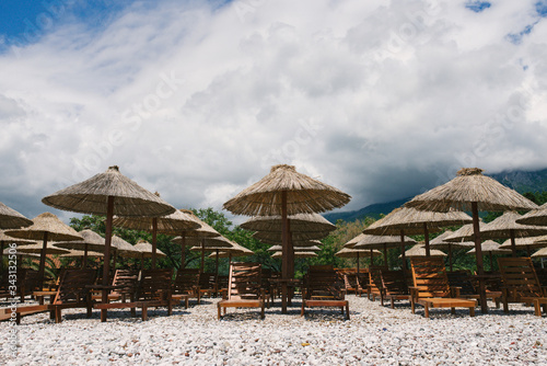 Sunbeds and umbrellas on a deserted pebble beach in cloudy weather on a background of clouds in Budva  Montenegro.