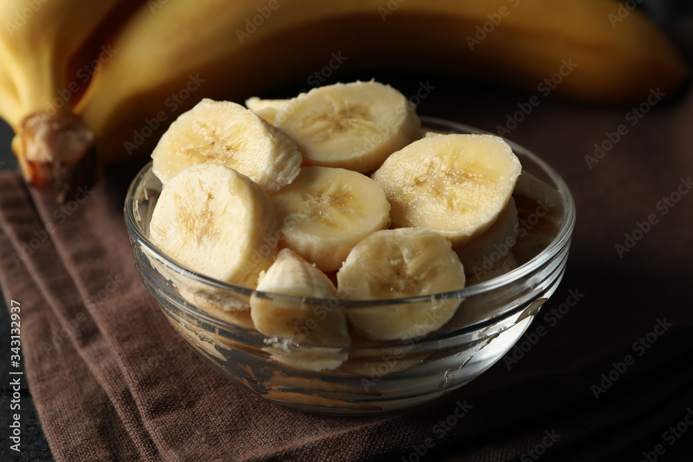 Bowl of banana slices, banana and towel on wooden background