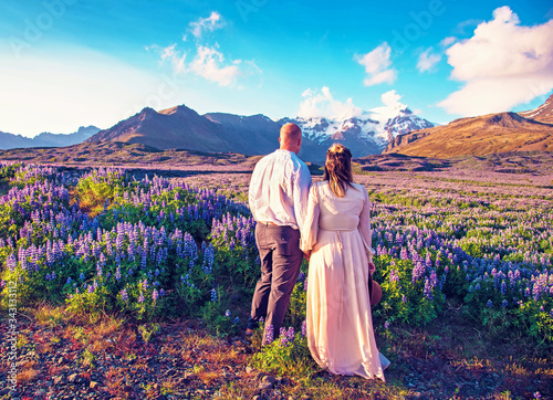 Obraz na płótnie Beautiful landscape with oung couple in lupine flowers on a background of mountains in Iceland. Magical places. Exotic countries. w salonie