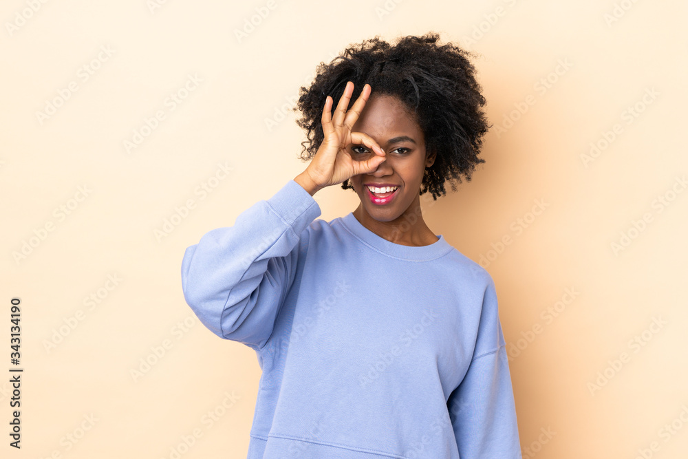 Young African American woman isolated on beige background showing ok sign with fingers Young African American woman isolated on beige background showing ok sign with fingers