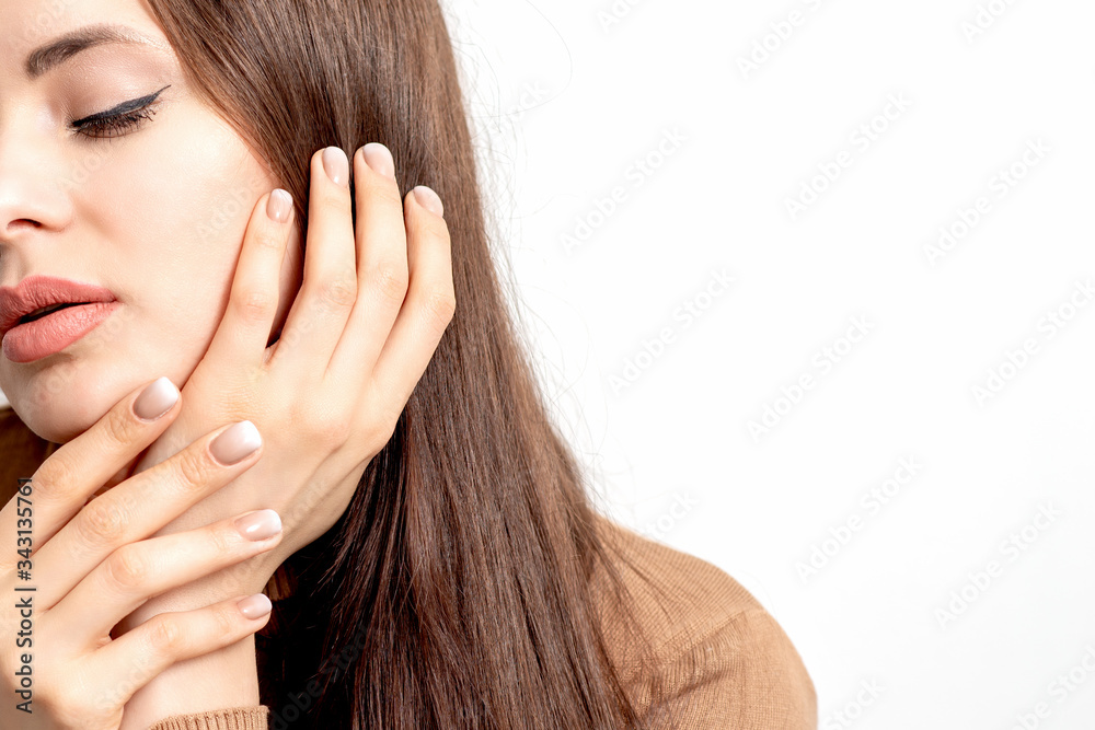 Portrait of pretty young woman touching face with her hand beige manicure on white background with copy space. Portrait of pretty young woman touching face with her hand beige manicure on white background with copy space.