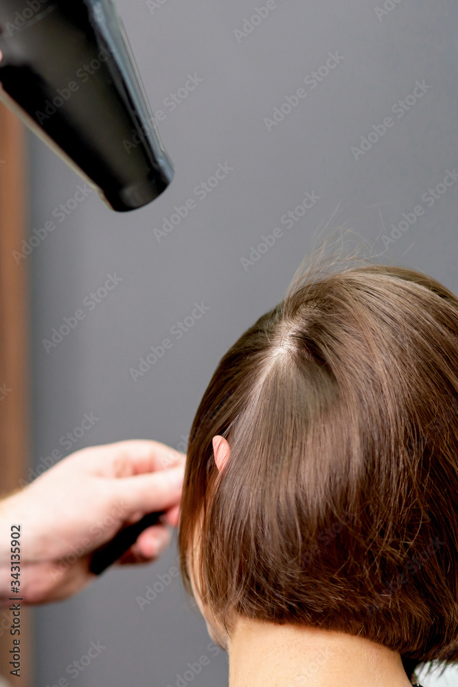 Fototapeta premium Close up of professional hairdresser is drying hair of woman, back view in hair salon.