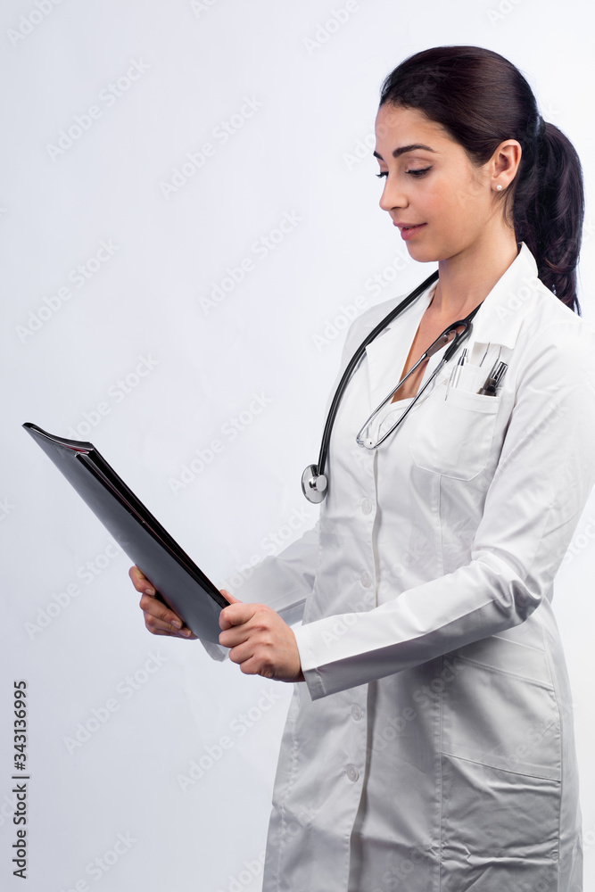 Dottoressa, con stetoscopio al collo camice bianco e un cartella in mano guarda il referto , isolata su sfondo bianco Dottoressa, con stetoscopio al collo camice bianco e un cartella in mano guarda il referto , isolata su sfondo bianco