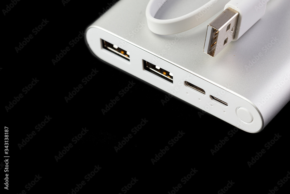 An additional stand-alone power bank for charging mobile devices. External battery isolated on a black background. White charger for smartphone, power supply (battery bank). Selective focus. An additional stand-alone power bank for charging mobile devices. External battery isolated on a black background. White charger for smartphone, power supply (battery bank). Selective focus.