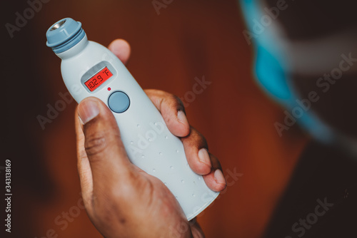 African american man using a temporal thermometer to record his temperature by running it across his forehead, man wearing surgical mask