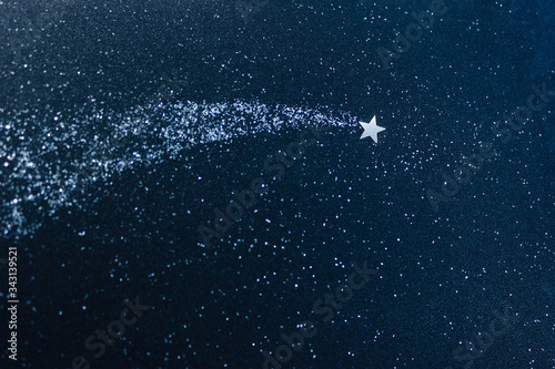 Silver confetti applique on a dark blue glitter of cardboard. Shooting star and stardust. The concept of a dream and make a wish. Selective focus.