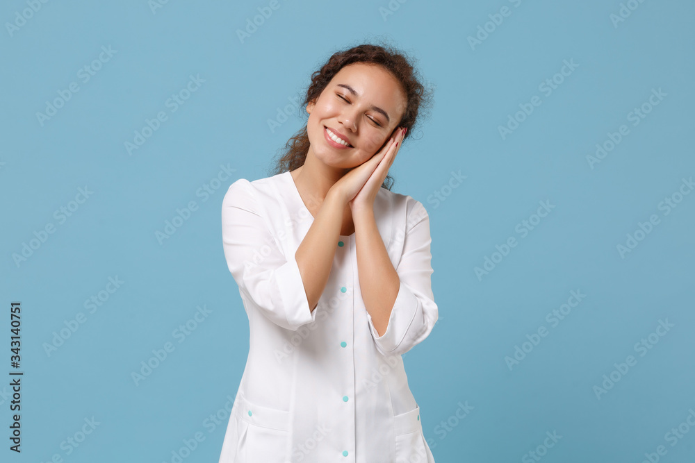 African american doctor woman isolated on blue background. Female doctor in white medical gown sleep with folded hands under cheek. Healthcare personnel health medicine concept. Mock up copy space. African american doctor woman isolated on blue background. Female doctor in white medical gown sleep with folded hands under cheek. Healthcare personnel health medicine concept. Mock up copy space.