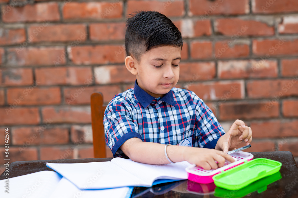 Cute little male student in school uniform writing on notebook while attending class in Primary school. He is using pencil box . Cute little male student in school uniform writing on notebook while attending class in Primary school. He is using pencil box .
