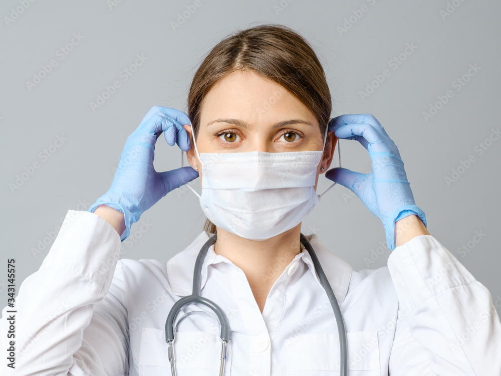 Portrait of doctor putting sterile mask isolated on gray Portrait of doctor putting sterile mask isolated on gray