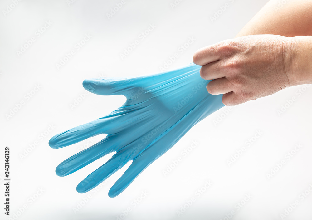 Obraz premium Woman pulls on her hand a blue latex medical glove on a white background. Horizontal orientation.