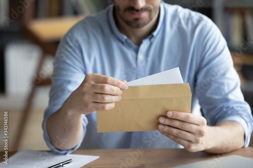 Focused businessman reading letter, looking at paper, holding envelope in hands close up, received news or important information, freelancer working with correspondence, sitting at work desk photo