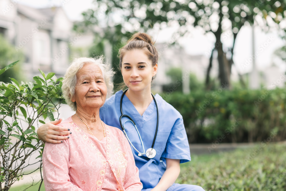 Nurse caregiver embracing happy Asian elderly woman outdoor in the park. Focused on eldery woman