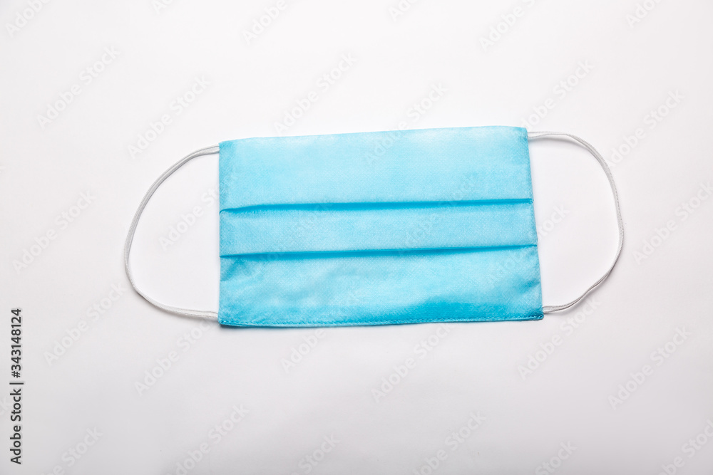 An even new medical disposable blue mask lies on a table on a white background. Horizontal orientation. An even new medical disposable blue mask lies on a table on a white background. Horizontal orientation.