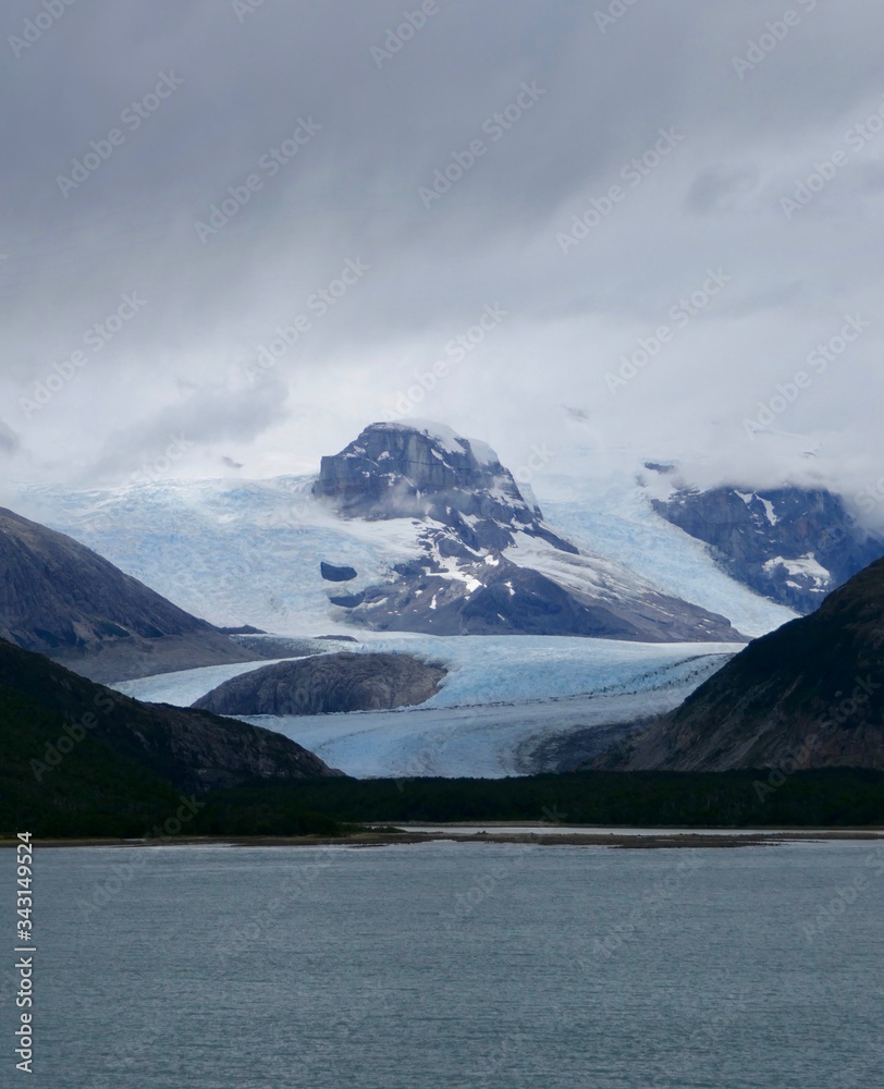 Glacier in chilean fjord with blue ice, high mountain and clouds, glacier alley, Beagle Channel