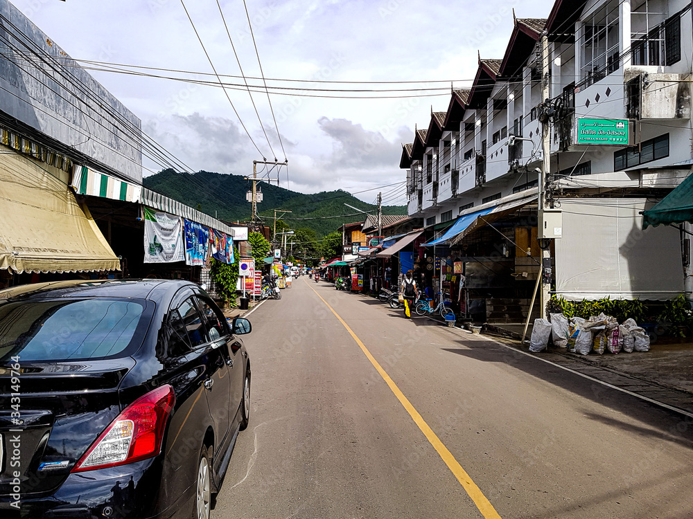 Fototapeta premium Car street road electricity cable mast houses village pai middle centre shops walking north chiang mai mountain green